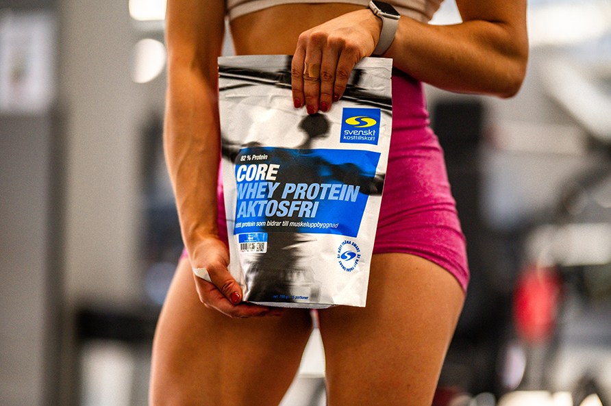 En kvinde str med en pose Core Whey Protein Laktosefri i sine hnder.